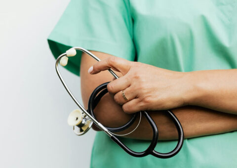 folded arms of a female medical professional with hand holding stethoscope